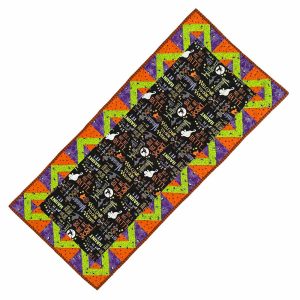 Cotton table runner with various spooky sentiments in bright orange, lime green, and purple on a black background. Measures 18x43 inches.