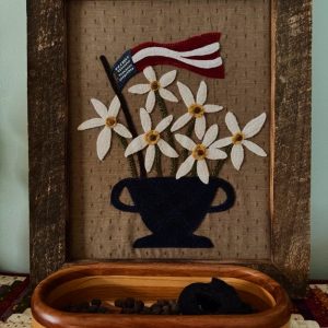 Summer Patriotic Centerpiece, brown wooden frame with tan background white flowers with yellow centers in a blue pot, red white and blue flag with flowers