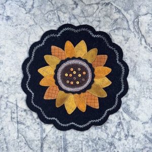 Navy blue wool circle with shades of orange petals in the shape of a sunflower with a brown center and buttons on a blue marble background