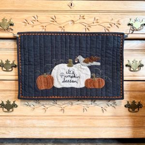 "Pumpkin Season" Wool Wall Quilt 20 x 13, blue mat with white and orange pumpkins with green stems and vines, grey bird with acorn in mouth. It's Pumpkin Season in cursive on white pumpkin